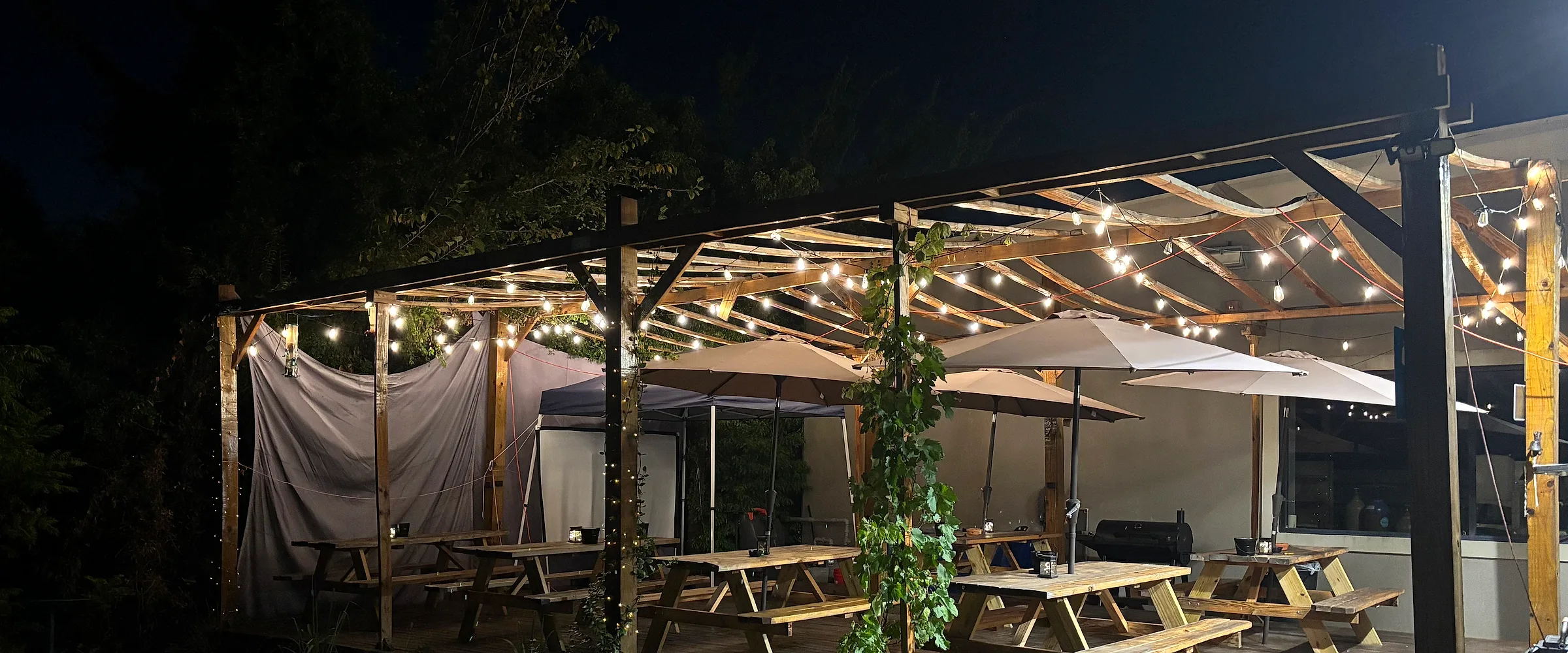 The Curry Creations patio after dark — a wooden pergola strung with warm lights over picnic tables and umbrellas